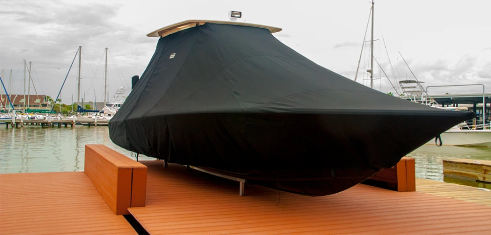 A center-console boat under a fitted black full cover on its lift at a marina dock