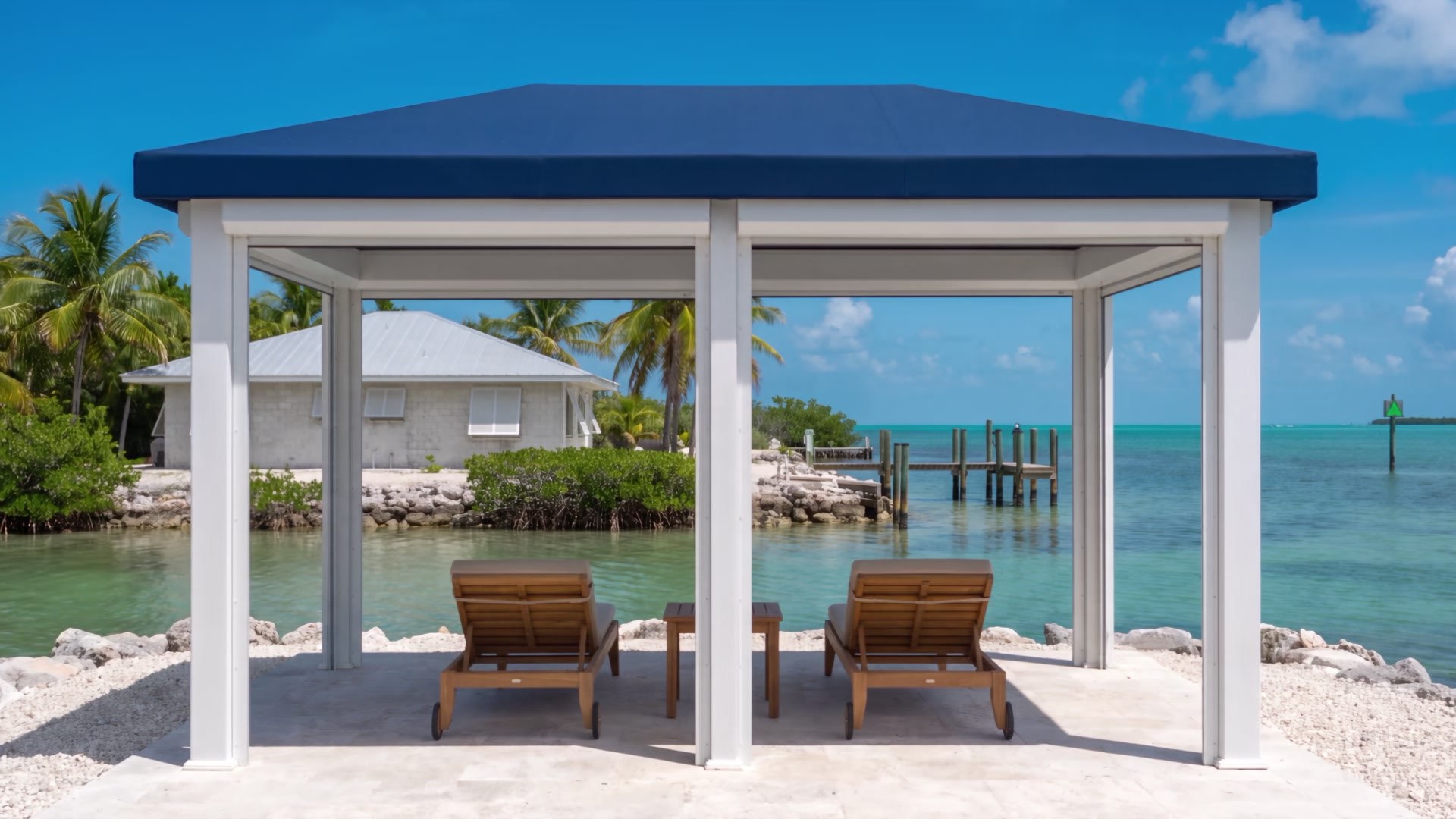 An open white waterfront cabana with a navy canvas roof and two wood lounge chairs