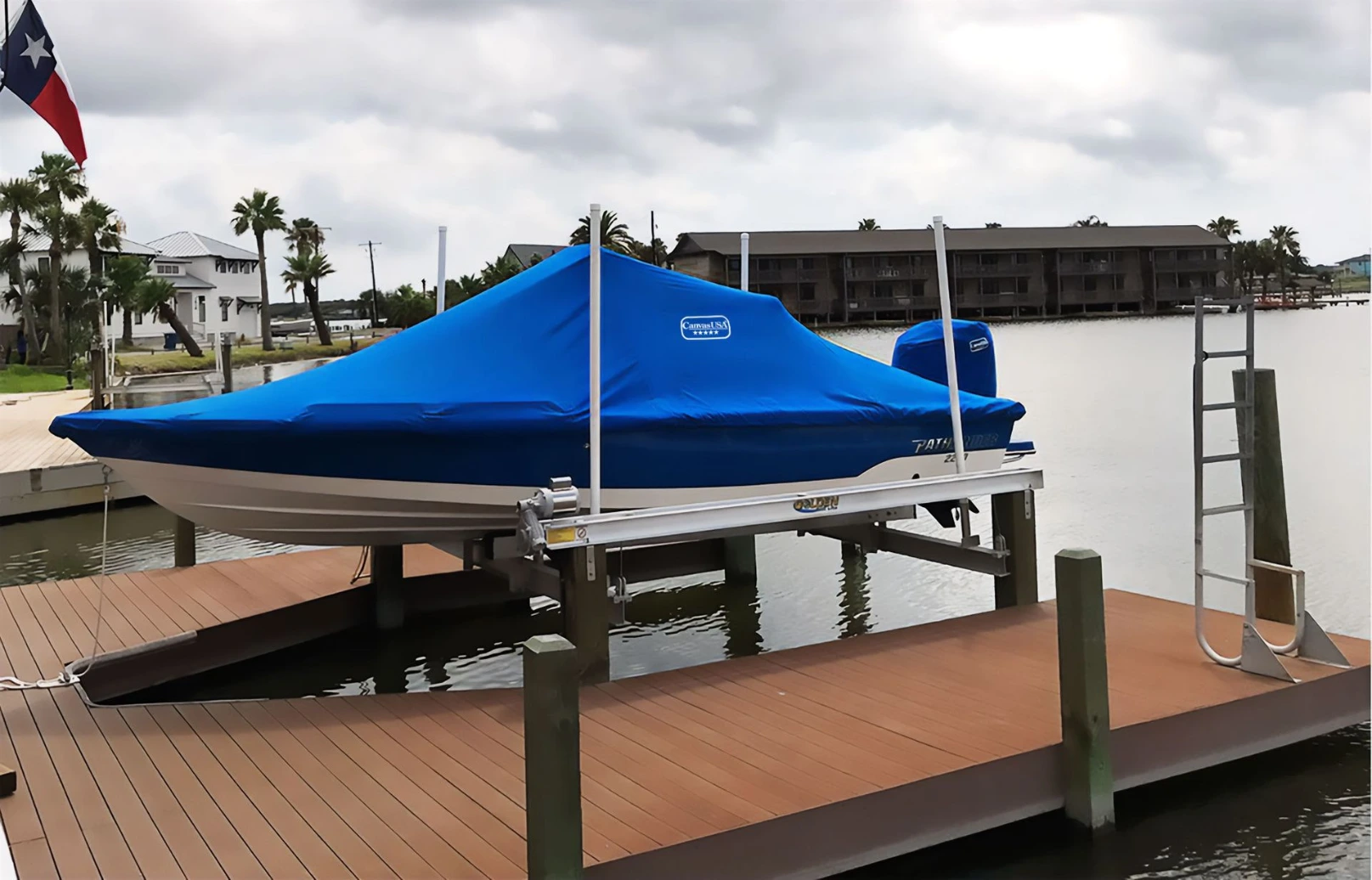 A boat under a fitted blue Canvas USA® full cover with a separate motor cover, hanging on its lift