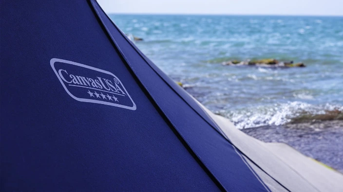 The Canvas USA® logo on a navy boat cover by the water