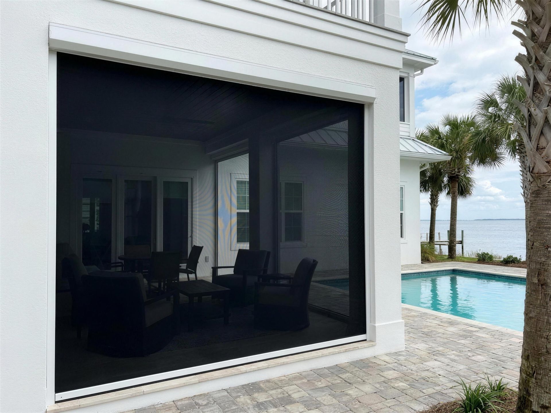 Black mesh drop screen lowered across a covered patio by the pool