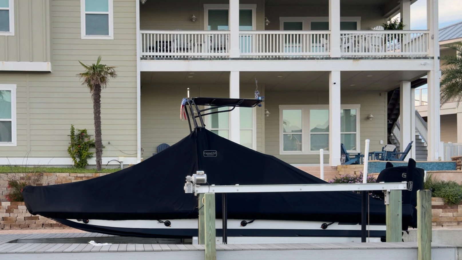An SCB center console under a fitted black Canvas USA® boat lift cover beside a waterfront home