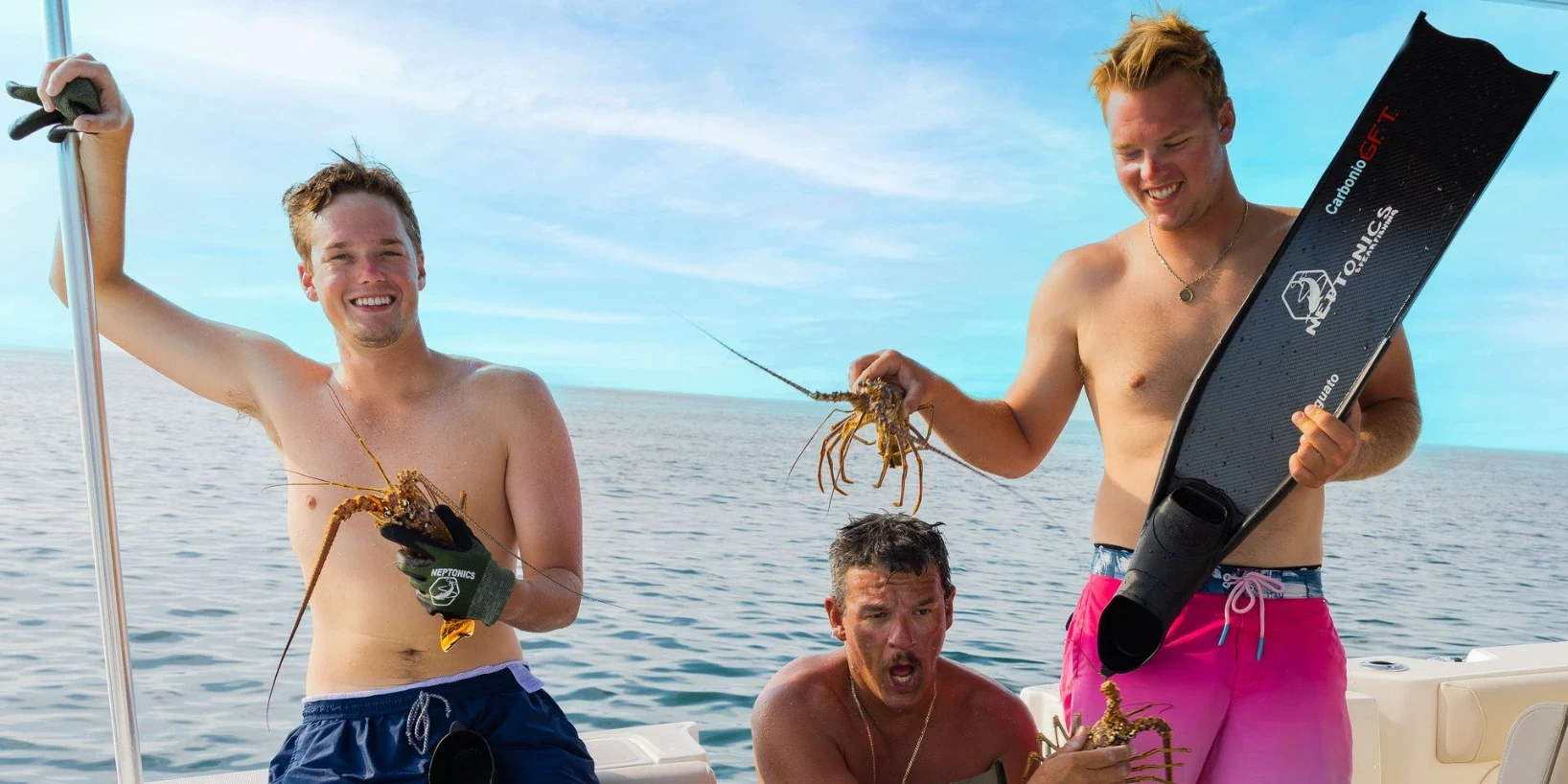 Three friends on a boat holding spiny lobsters after a dive